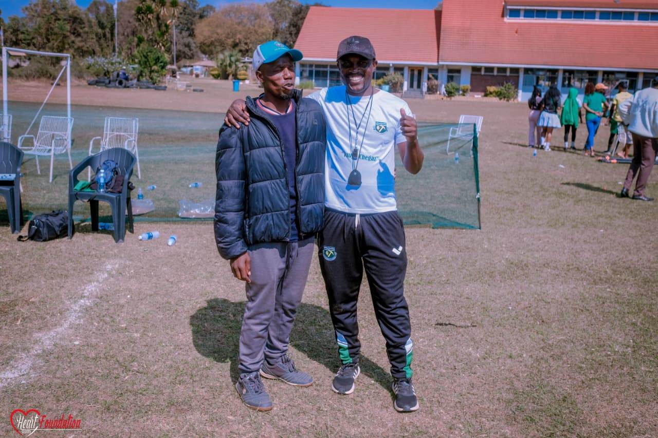 A coach in club training top giving a thumbs-up pitchside